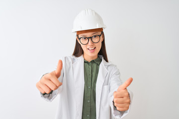 Poster - Young chinese engineer woman wearing coat helmet glasses over isolated white background approving doing positive gesture with hand, thumbs up smiling and happy for success. Winner gesture.