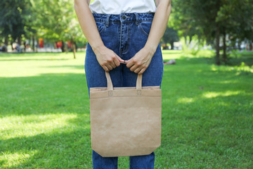 Young woman holding tote bag against greenery background, empty space