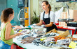 © JackF - Portrait of friendly female fishmonger showing raw European bass to woman behind counter of seafood store