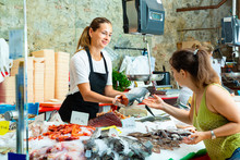 Polite  Female Worker Of Fish Shop In Apron Offering Fresh Raw Salmon To Woman Customer
