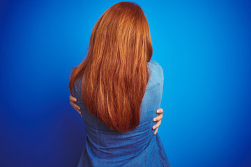 Sticker - Young beautiful redhead woman wearing denim shirt standing over blue isolated background Hugging oneself happy and positive from backwards. Self love and self care