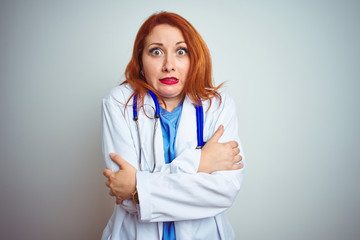 Sticker - Young redhead doctor woman using stethoscope over white isolated background shaking and freezing for winter cold with sad and shock expression on face