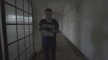 A Scary Ghost Of A Fat Woman With A Rusty Cage On His Head And With Shackles On His Hands Appears Behind A Tourist In The Gloomy Corridor Of An Old Abandoned Psychiatric Hospital.