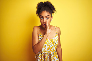 Sticker - African american woman wearing casual floral dress standing over isolated yellow background hand on mouth telling secret rumor, whispering malicious talk conversation