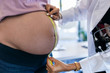 © nenetus - Pregnant woman exposing her belly while doctor using a measuring tape to follow the growth of the baby at a hospital.