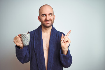 Sticker - Young man wearing a bathrobe drinking a cup of coffee in the morning over isolated background very happy pointing with hand and finger to the side