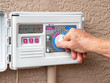 Automatic electric outdoor irrigation timer. Closeup of male hand setting programmable lawn watering system.