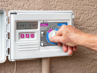 Automatic electric outdoor irrigation timer. Closeup of male hand setting programmable lawn watering system.