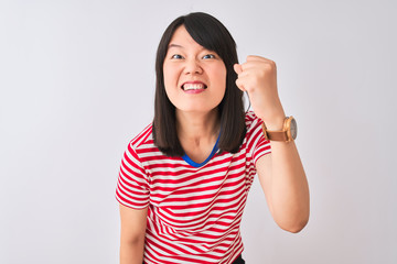 Wall Mural - Young beautiful chinese woman wearing red striped t-shirt over isolated white background angry and mad raising fist frustrated and furious while shouting with anger. Rage and aggressive concept.