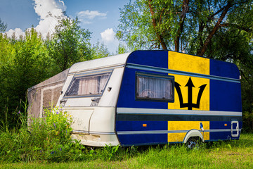 A car trailer, a motor home, painted in the national flag of  Barbados stands parked in a mountainous. The concept of road transport, trade, export and import between countries.