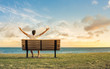 © kieferpix - Young man sitting on park bench feeling happy and free.