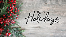 Happy Holidays Text With Holiday Evergreen Branches And Berries Over Rustic Wooden Background