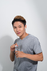 Wall Mural - Young sports Asian man wearing earphones and holding water bottle on white background.