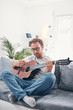 © astrosystem - Man playing acoustic guitar in the living room.
