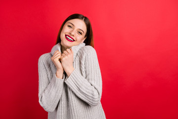 Poster - Pretty overjoyed lady touching hands soft knitted sweater isolated on red background