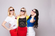 © Вячеслав Косько - Three cheerful women wearing bright colorful skirts, shirts and glasses standing on grey isolated background. Happy girls looking at camera, laughing and showing tongue. Concept of happiness.