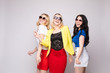 © Вячеслав Косько - Three cheerful women wearing bright colorful skirts, shirts and glasses standing on grey isolated background. Happy girls looking at camera, laughing and showing tongue. Concept of happiness.
