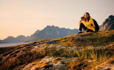 Happy girl traveler with a camera in his hands in Norway, on the Lofoten Islands admires the sunset