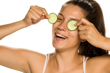 Canvas Print - Young smiling woman posing with slices of cucumbers on her eyes on white background