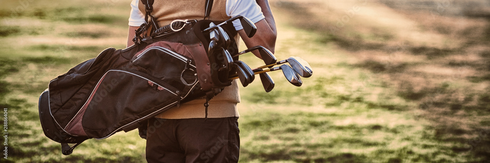 Man carrying golf bag while standing on field - obrazy, fototapety, plakaty 