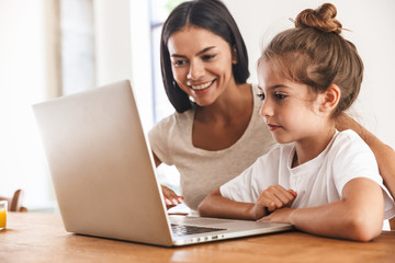 Wall Mural - image of attractive family woman and her little daughter smiling and using laptop computer together 