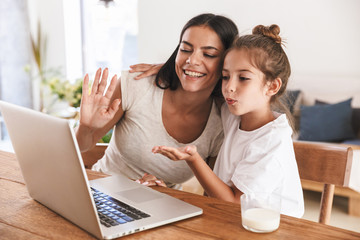 Wall Mural - image of happy family woman and her little daughter smiling and waving at laptop computer together i