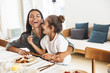 Image of cheerful family mother and little daughter smiling and eating together while having breakfast at home in morning