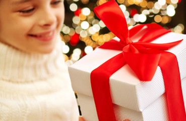 Poster - childhood, holidays and people concept - happy beautiful girl with christmas gift box over festive lights background