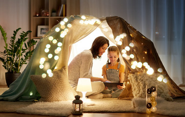 Poster - family, hygge and technology concept - happy mother and little daughter with tablet pc computer in kids tent at night at home