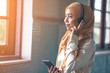 © rachaphak - Portrait of a smiling young modern arabian woman holding mobile phone and listening the music to headphone.