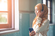 © rachaphak - Portrait of a smiling young modern arabian woman closing eyes, holding mobile phone and listening the music to headphone.