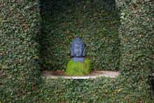 Black Stone Sculpture Of A Buddha Head In A Green Plant Niche In A Garden