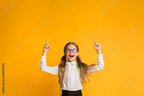 Fotomural Excited School Girl Pointing Fingers Up Over Yellow Background, Copyspace