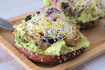 healthy brunch in a  wooden dish in table with veggie bagle with avocado, tomato, olives, outbreaks and olive oil. 