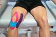 The two knees of a patient, one of them with three medical ribbons, purple, light blue and pink. Concept of muscle health and relaxation.