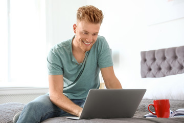 Wall Mural - Young man using laptop while sitting on bed at home