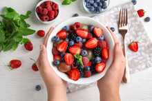 Woman Holding Bowl With Fresh Tasty Fruit Salad Over White Wooden Table, Top View