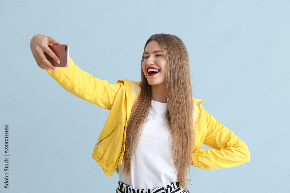 Happy young woman taking selfie on color background