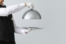 Handsome Waiter With Tray And Cloche On Light Background
