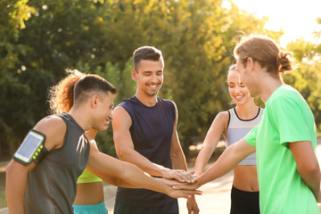 Group of sporty young people putting hands together outdoors