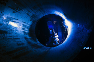 Welding of large pipes by industrial workers wearing safety equipment and dark glass to prevent sparks and light in Asia.