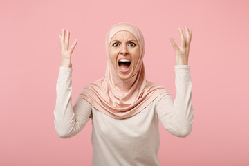 Canvas Print - Shocked irritated arabian muslim woman in hijab light clothes posing isolated on pink background. People religious Islam lifestyle concept. Mock up copy space. Screaming, swearing, spreading hands.