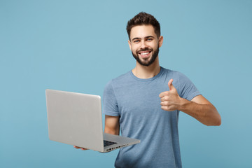 Young smiling attractive man in casual clothes posing isolated on blue wall background, studio portrait. People lifestyle concept. Mock up copy space. Holding laptop pc computer, showing thumb up.