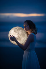 Wall Mural - delicate image of an angel, a girl with the moon in her hands on the night beach. artistic photograp