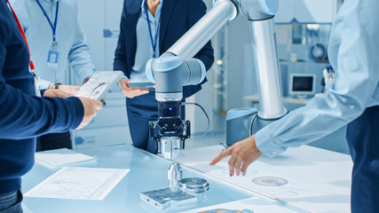 Aufkleber - Team of Industrial Robotics Engineers Gathered Around Table With Robot Arm, They Use Tablet Computer to Manipulate and Program it to Pick Up and Move Metal Component. Focus on Hands