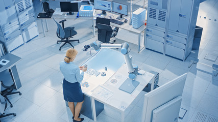 Aufkleber - Stylish Female Industrial Robotics Engineer Looks at Blueprints Engineering Ways to Program and Manipulate Robot Arm for Lifting, Moving Objects. Technology Research Facility for Cloud Computing