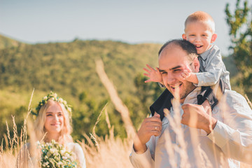 Happy family with kid walking together in wheat field on warm and sunny summer day. Soft focus.