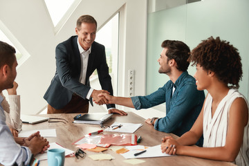 Celebrating success Two cheerful colleagues shaking hands and smiling while sitting in the modern office