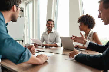 Analyzing results. Young man in formal wear holding financial reports and discussing it with team while sitting at the office table