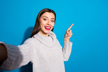 Sticker - Photo of pretty lady making selfies indicating arm empty space wear warm knitted pullover isolated blue background